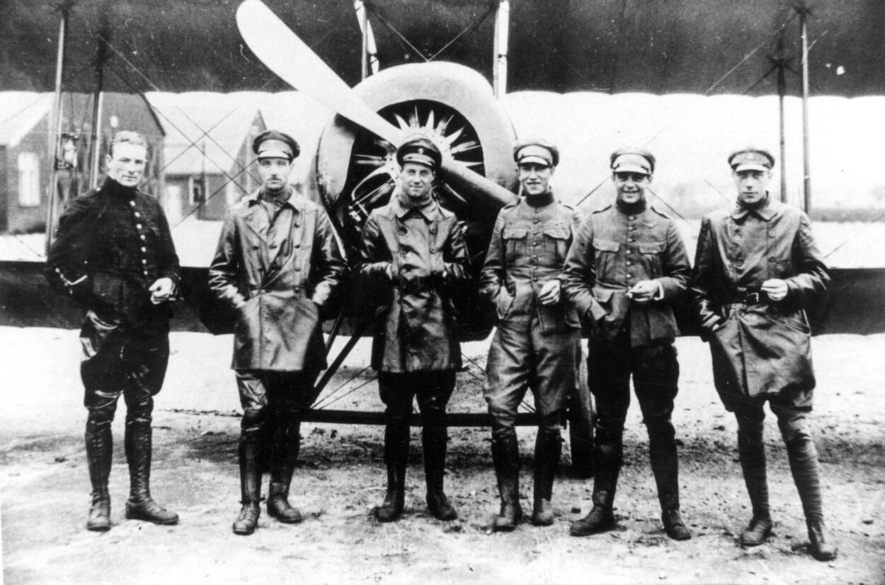 Zwart-wit groepsfoto. Een groep vliegers in uniform staan voor een militair vliegtuig.