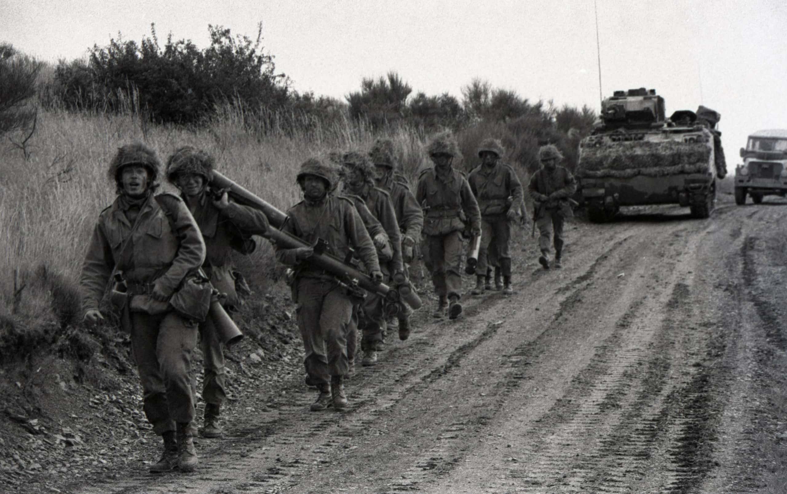 Zwart-wit foto. Een groep militairen in uniform marcheert buiten.