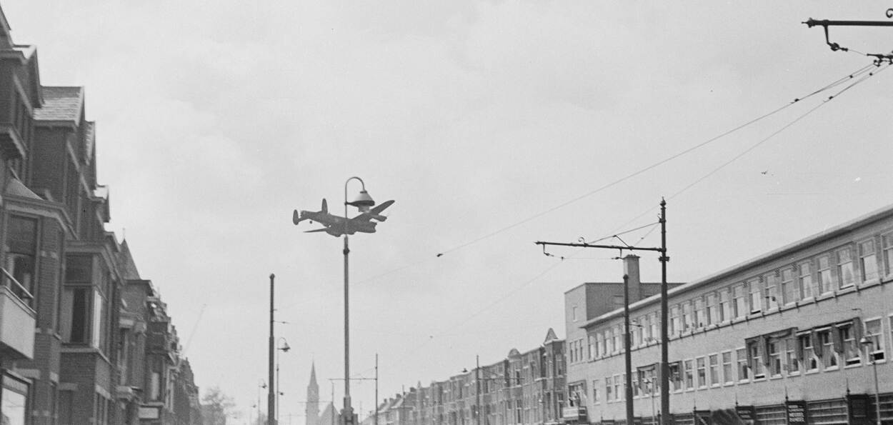 Zwart-witfoto van een vliegtuig in de lucht boven een straat.