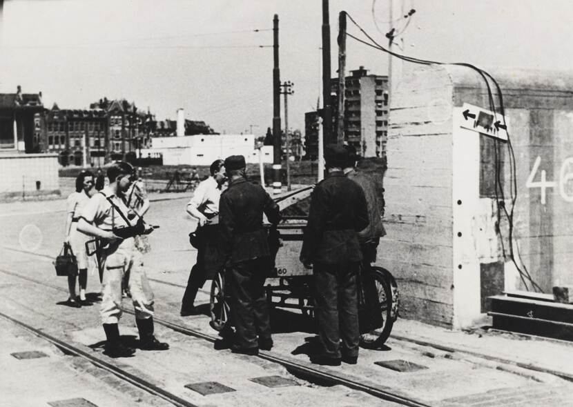 Zwart-witfoto, 2 Duitse militairen in uniform worden met een bakfiets staande gehouden door twee verzetslieden - 1 van hen met een geweer.