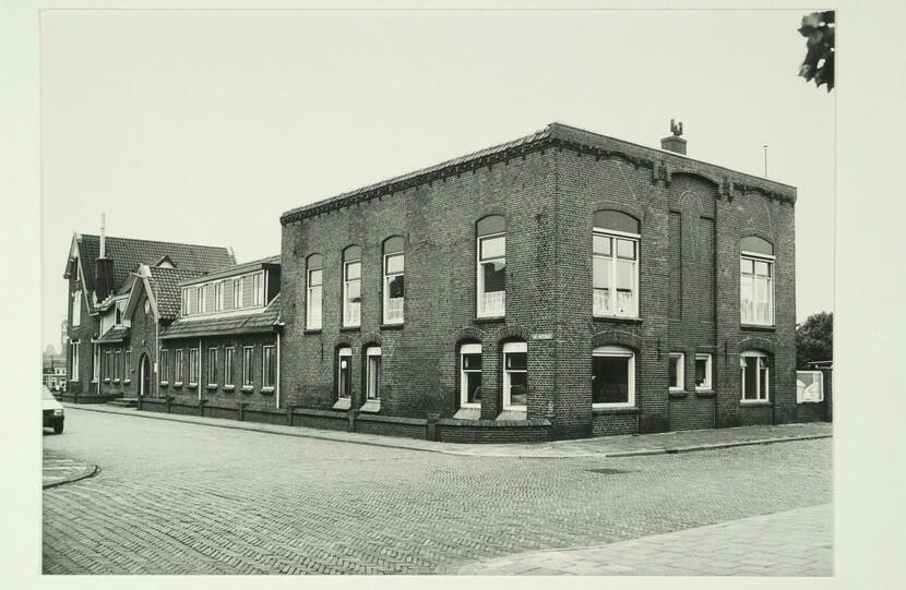 Zwart-witfoto van een vierkant gebouw op de hoek van een straat.