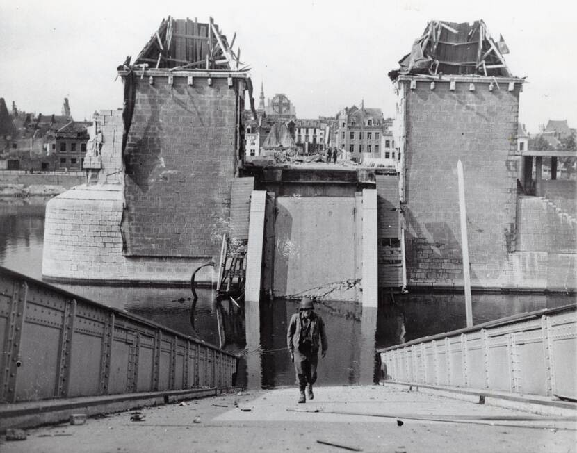 Zwart-witfoto van een in het water gestort wegdek van een brug, een militair loopt over het hellende wegdek omhoog.