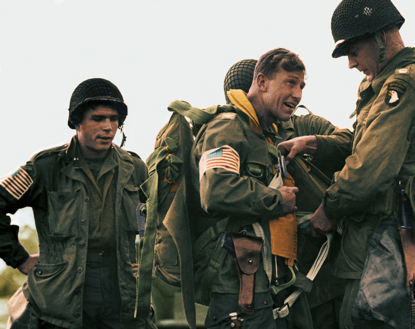 4 militairen in groene uniformen, 2 hebben een Amerikaanse vlag op de mouw,.