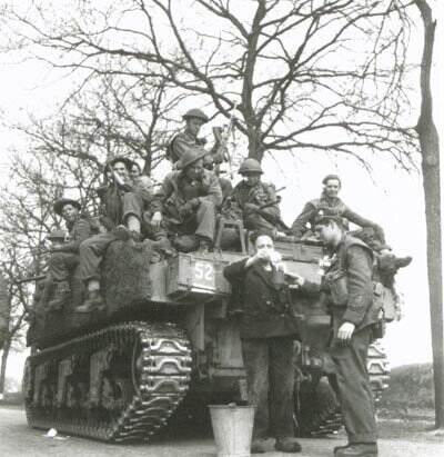 Zwart-witfoto, een Sherman tank vol met Canadese militairen, ervoor schenkt een boer een kopje melk in uit een emmer.