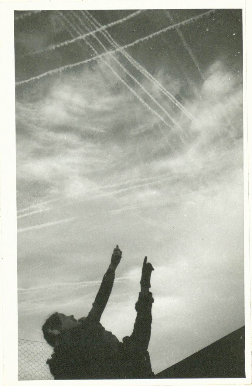 Zwart-witfoto, onderin twee figuren die omhoog wijzen en kijken, in een heldere lucht zijn meerdere kruisende condenssporen te zien.