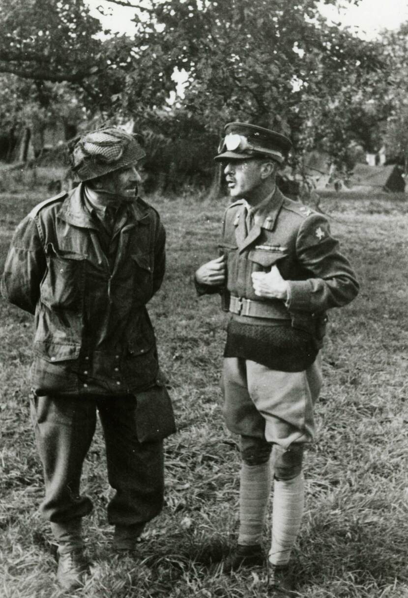 Zwart-witfoto van 2 mannen in uniform die met elkaar praten, ze staan in een veld.