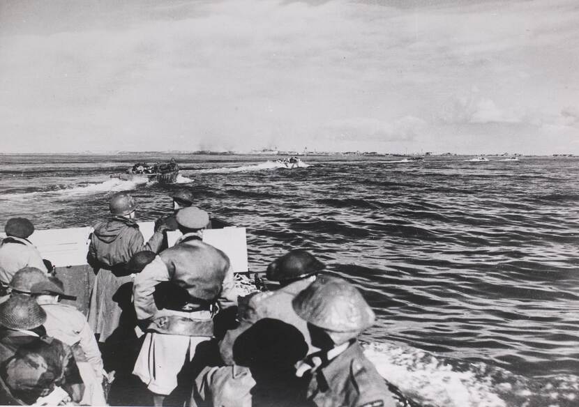 Zwart-witfoto vanaf een landingsvaartuig met militairen op zee, in de verte is de skyline van Vlissingen te zien.