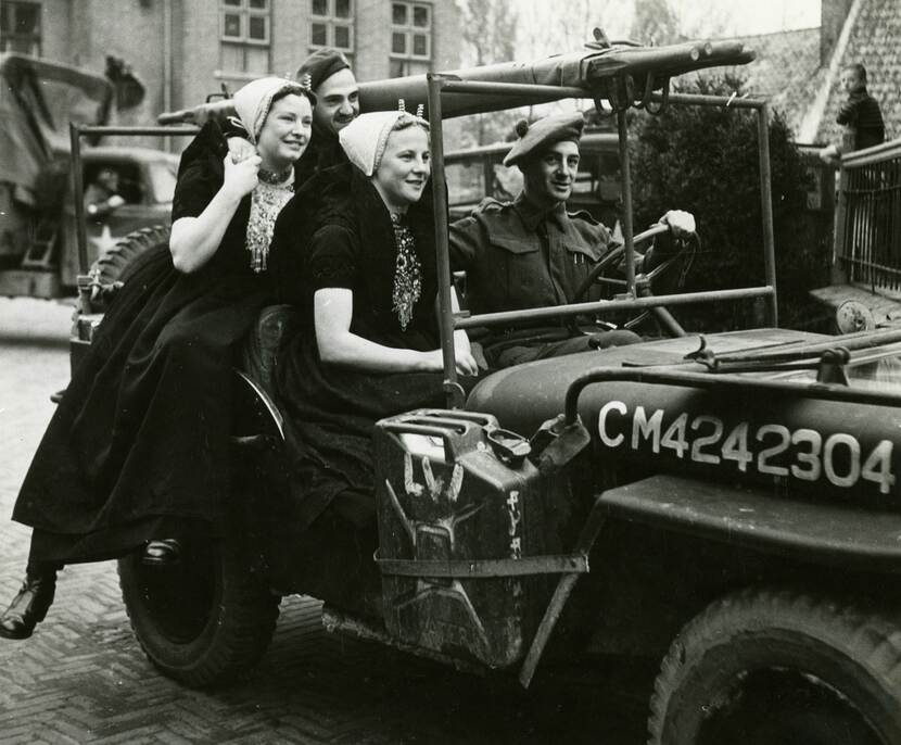 Zwart-witfoto van twee jonge vrouwen en twee militairen op een jeep, een van de militairen heeft zijn arm om een van de vrouwen geslagen.