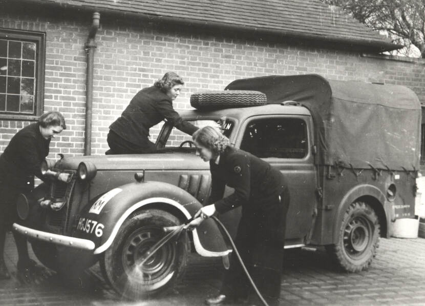 Zwart-witfoto van drie vrouwen in marine-uniform die een legerjeep wassen.