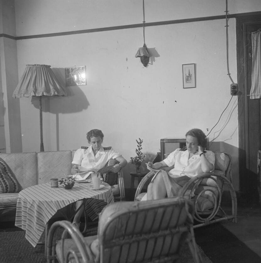 Zwart-witfoto van twee vrouwen in wit uniform die aan het lezen zijn in een zitkamer.