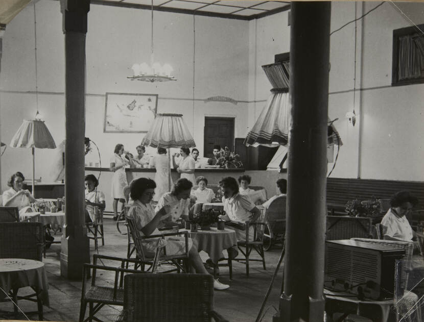 Zwart-witfoto van een grote zitkamer. Verschillende marva's zitten in uniform te lezen of staan bij de bar.