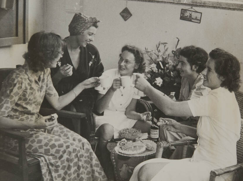 Zwart-witfoto, 5 vrouwen toosten in een zitkamer met koppen thee of koffie en taart. In het midden zit Van Straten in wit uniform. Nog 1 andere vrouw is in uniform.