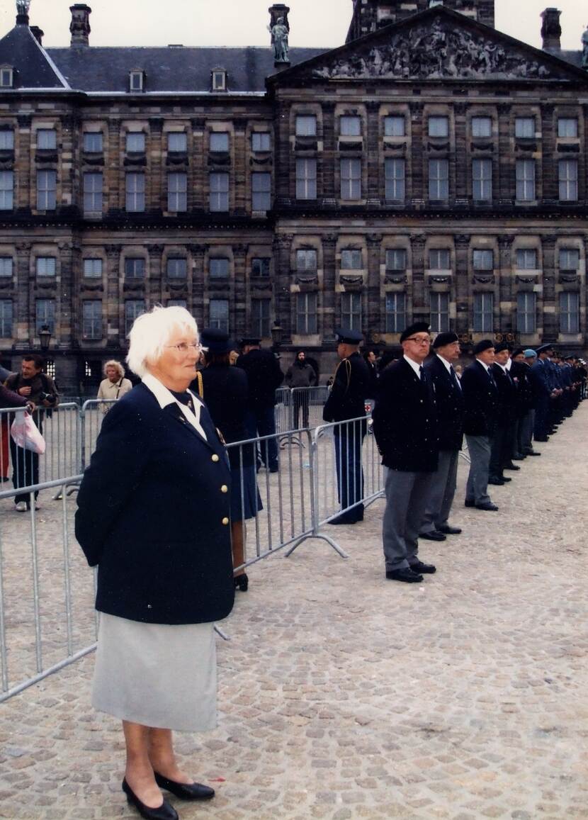 Kleurenfoto, Cools-van Straten staat aangetreden als inmiddels oudere vrouw, in marine-uniform. Naast haar staan mannelijke veteranen opgesteld.