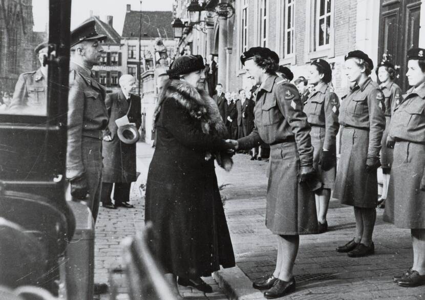 Zwart-witfoto, Een lid van het VHK schudt de hand van koningin Wilhelmina, achter haar staan VHK'sters opgesteld, eromheen staan toeschouwers.