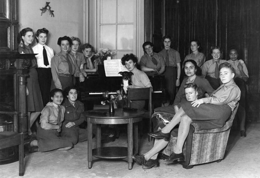 Zwart-witgroepsfoto van 16 vrouwen in militair uniform, rond een piano. De vrouw die achter de piano zit heeft een hond op schoot.