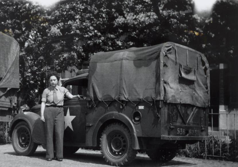 Zwartwit-foto van een vrouw in militair uniform naast een vrachtwagen.