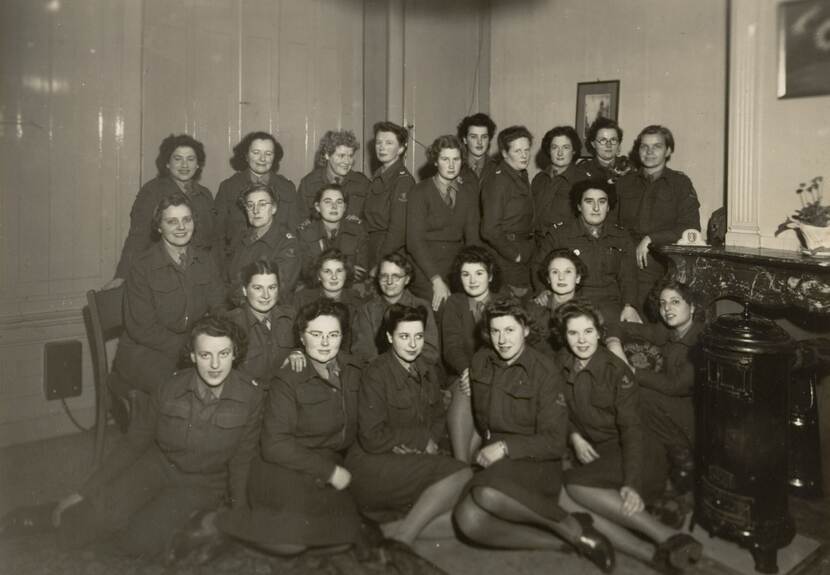 Zwart-wit foto. Een groep vrouwen in uniform poseert voor de camera. De foto is gemaakt in de setting van een kamer.