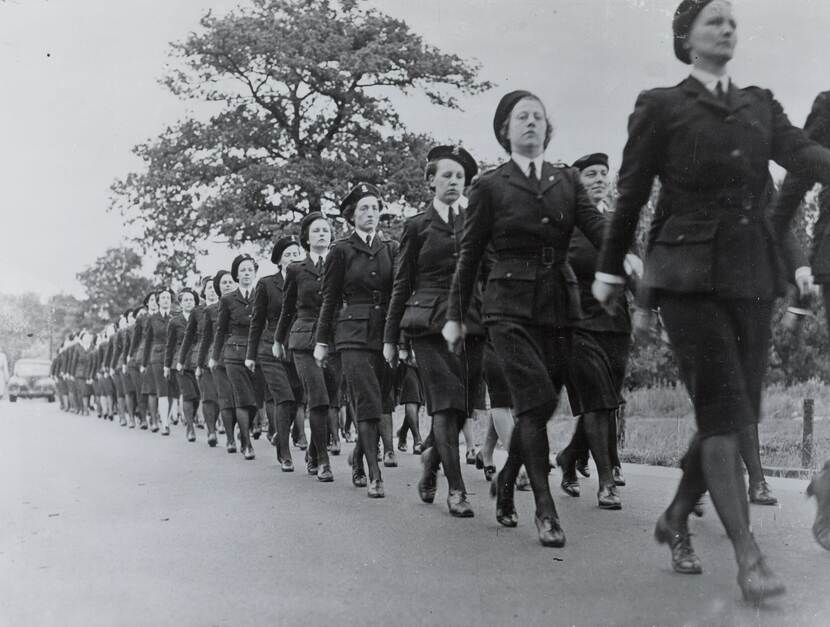 Zwart wit-foto. De foto is gemaakt vanaf de grond. Te zien is hoe een groep vrouwen in uniform in looppas voorbij komt.