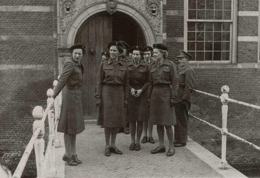 Zwart-wit foto. Een groep vrouwelijke militairen staat op een brug voor een poort van een gebouw.