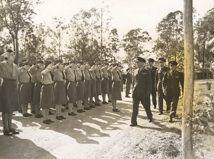 Zwart-witfoto, vrouwen in militair uniform staan opgesteld terwijl mannelijke militairen langs hen lopen.