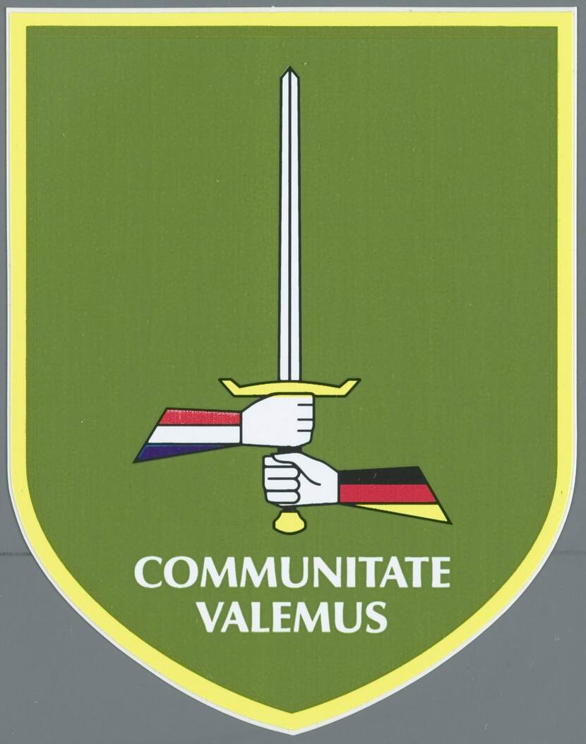 Groene achtergrond, een zwaard vastgehouden door twee handen, de arm links heeft op de mouw de Nederlandse vlag, de rechter de Duitse vlag, hieronder staat de tekst 'communitate valemus'.