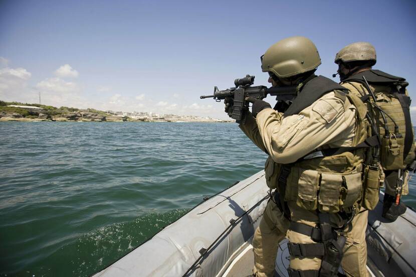 2 militairen in een rubberboot op zee, één houdt een geweer vast, op de achtergrond is Mogadishu te zien.