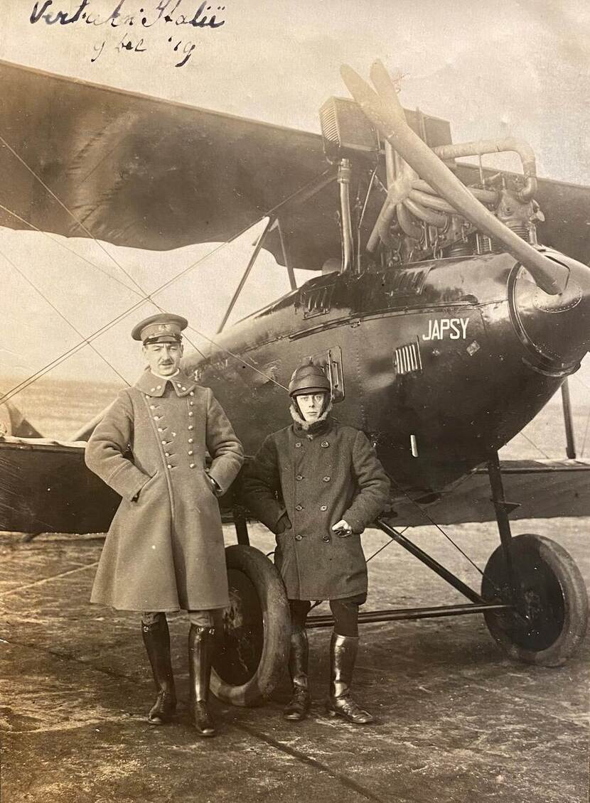 Zwart-witfoto van twee militairen voor een dubbeldeks propellervliegtuig. Op de foto staat handgeschreven 'Vertrek Italië 9-12-1919'.