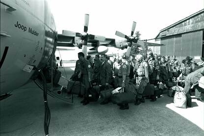 Zwart-witfoto, een groep militairen met bepakking is bezig in te stappen in een vliegtuig, op het vliegtuig is de naam 'Joop Mulder' te lezen.