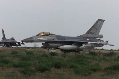 foto van een F-16 straaljager in een veld, onder de vleugel zijn meerdere raketten te zien, op de achtergrond staat een tweede F-16.