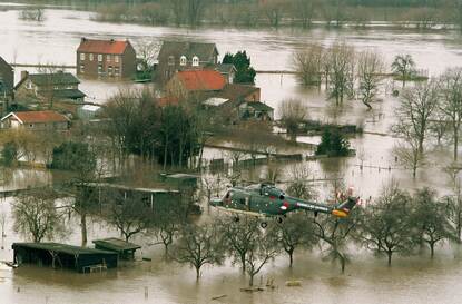 Luchtfoto van een helikopter boven onder water gelopen huizen langs een overstroomde rivier.