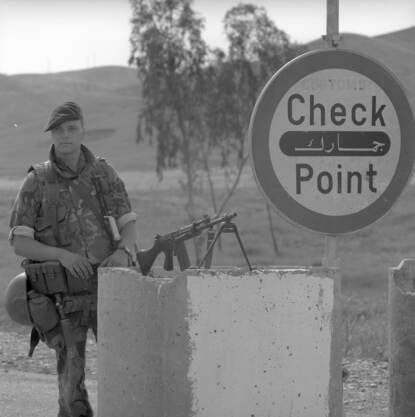 Zwart-witfoto, een marinier houdt de wacht naast een bord waar 'check point' op staat, voor zich heeft hij zijn geweer op een cementblok opgesteld.